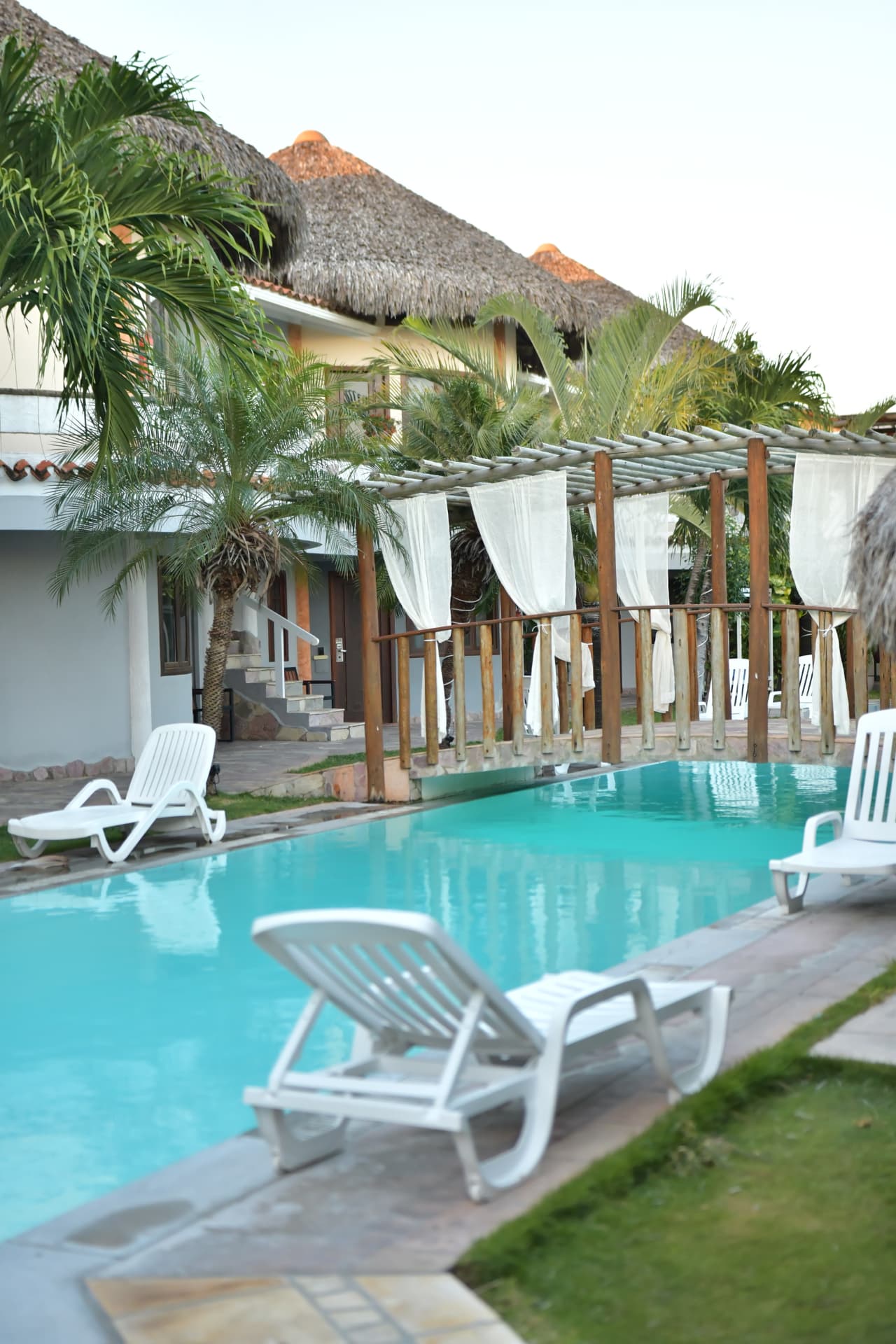 Piscina do hotel com espreguiçadeiras e pergolado de cortinas brancas