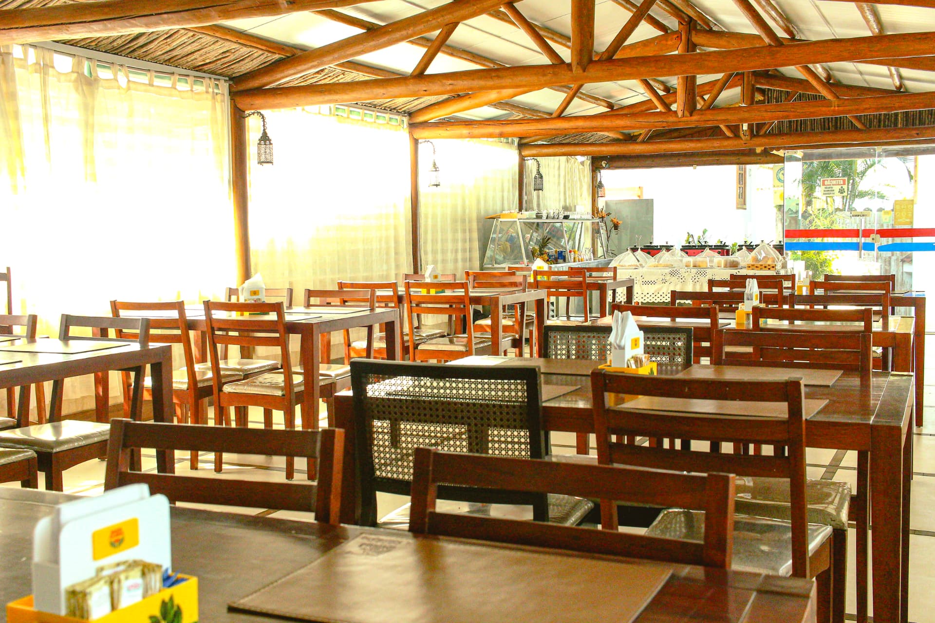 Salão do restaurante com teto de madeira, mesas e buffet ao fundo
